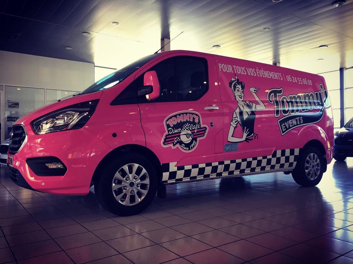 Véhicule rose floqué Tommy’s Events avec logo rétro, coordonnées et visuel diner américain