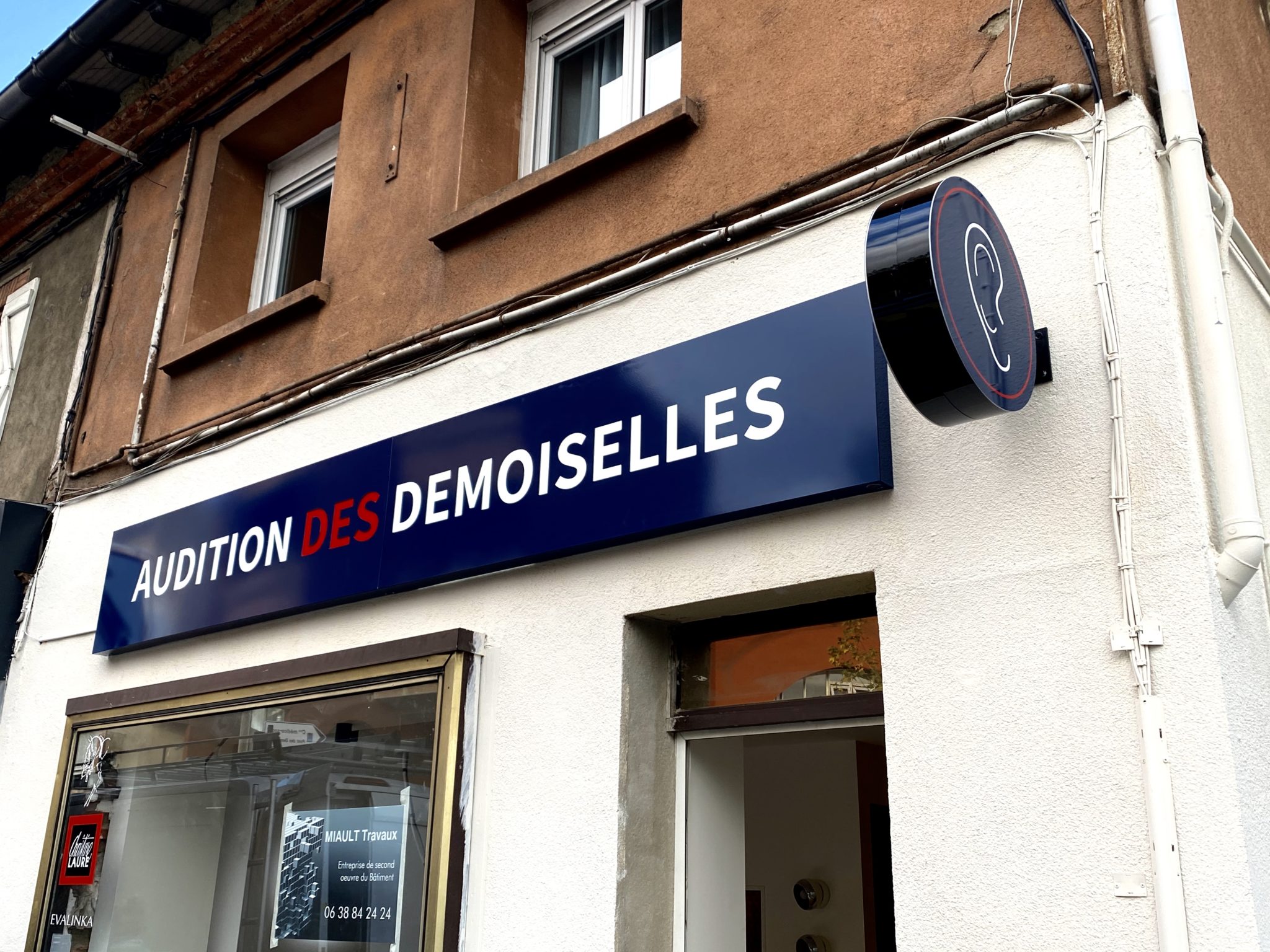 Façade Audition des Demoiselles avec enseigne lumineuse bleue et enseigne drapeau ronde