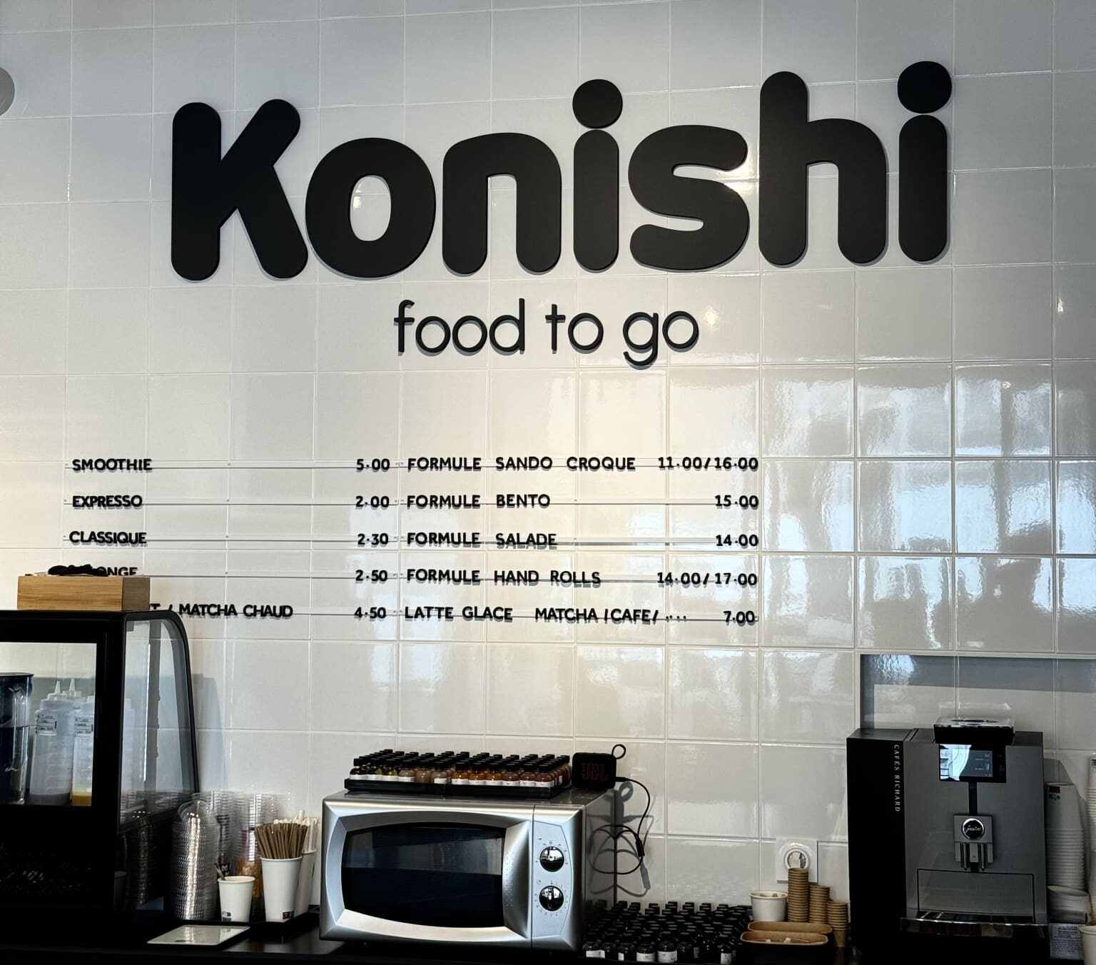 Lettrage mural Konishi Food to Go à Toulouse en lettres découpées noires sur carrelage blanc
